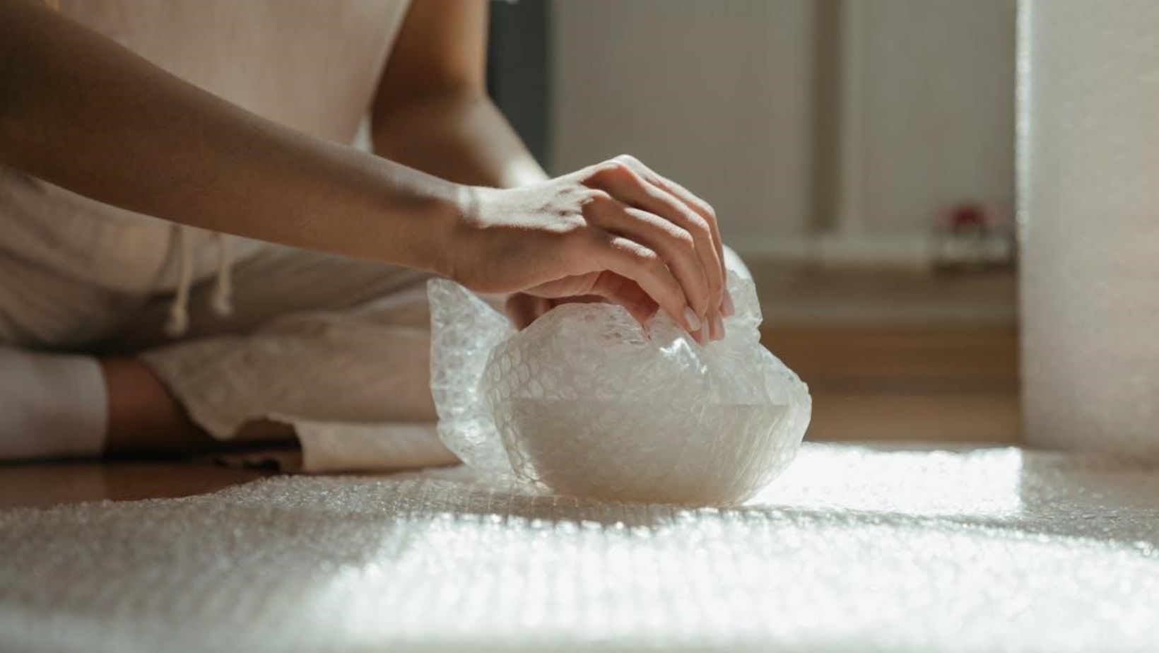 Woman wrapping a bowl in bubble wrap.